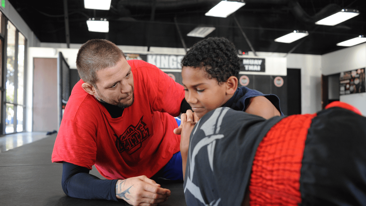 A school-aged child practicing Brazilian Jiu-Jitsu in a martial arts academy. The instructor is guiding the student, demonstrating the value of disciplined practice.